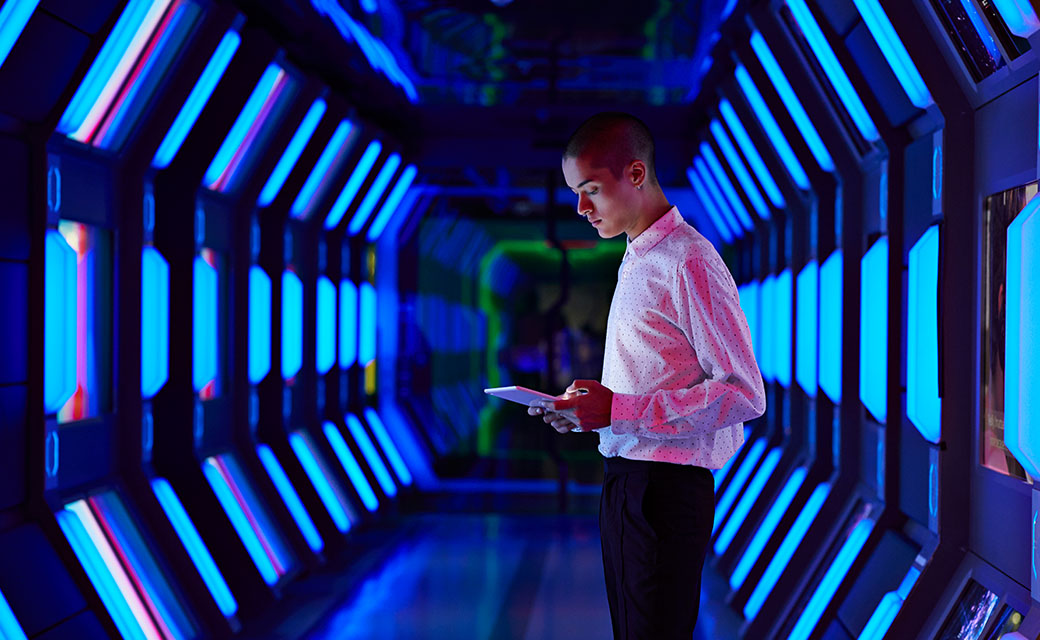 Man looking at an electronic device in a high-tech, futuristic hallway